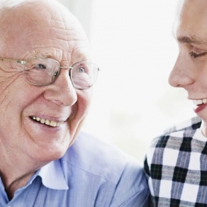 En äldre man skrattar tillsammans med hemtjänstpersonal. Foto.